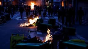 Des piétons passent devant des poubelles en feu après un concert de casseroles pour protester contre le discours télévisé du d'Emmanuel Macron, à Paris le 17 avril 2023