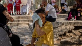 Une touriste s'essuie le visage avec une serviette devant le site monumental fermé de l'Acropole à Athènes, le 23 juillet 2025. 