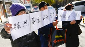 Des proches de passagers du vol MH370 de la Malaysia Airlines tiennent une pancarte sur laquelle on peut lire "Nous demandons fermement un procès public pour les affaires du vol MH370 de la Malaysia Airlines" près d'un tribunal de Pékin, le 27 novembre 2023. 