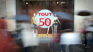Des piétons passent devant une vitrine avec un autocollant "Tout à -50%", au premier jour des soldes d'été à Paris, le 22 juin 2011.