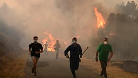 Des personnes courent près d'une zone incendiée lors d'un incendie de forêt près du village de Larouco, dans la province d'Ourense, au nord-ouest de l'Espagne, le 13 août 2025.