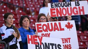 Des supporteurs avec des pancartes en soutien à l'équipe féminine de football du Canada, qui dénonce les inégalités femmes-hommes au sein de la fédération