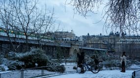 Des piétons se tiennent sur un parc enneigé à Paris, avec le pont de Bir Hakeim en arrière-plan, le 18 janvier 2024.