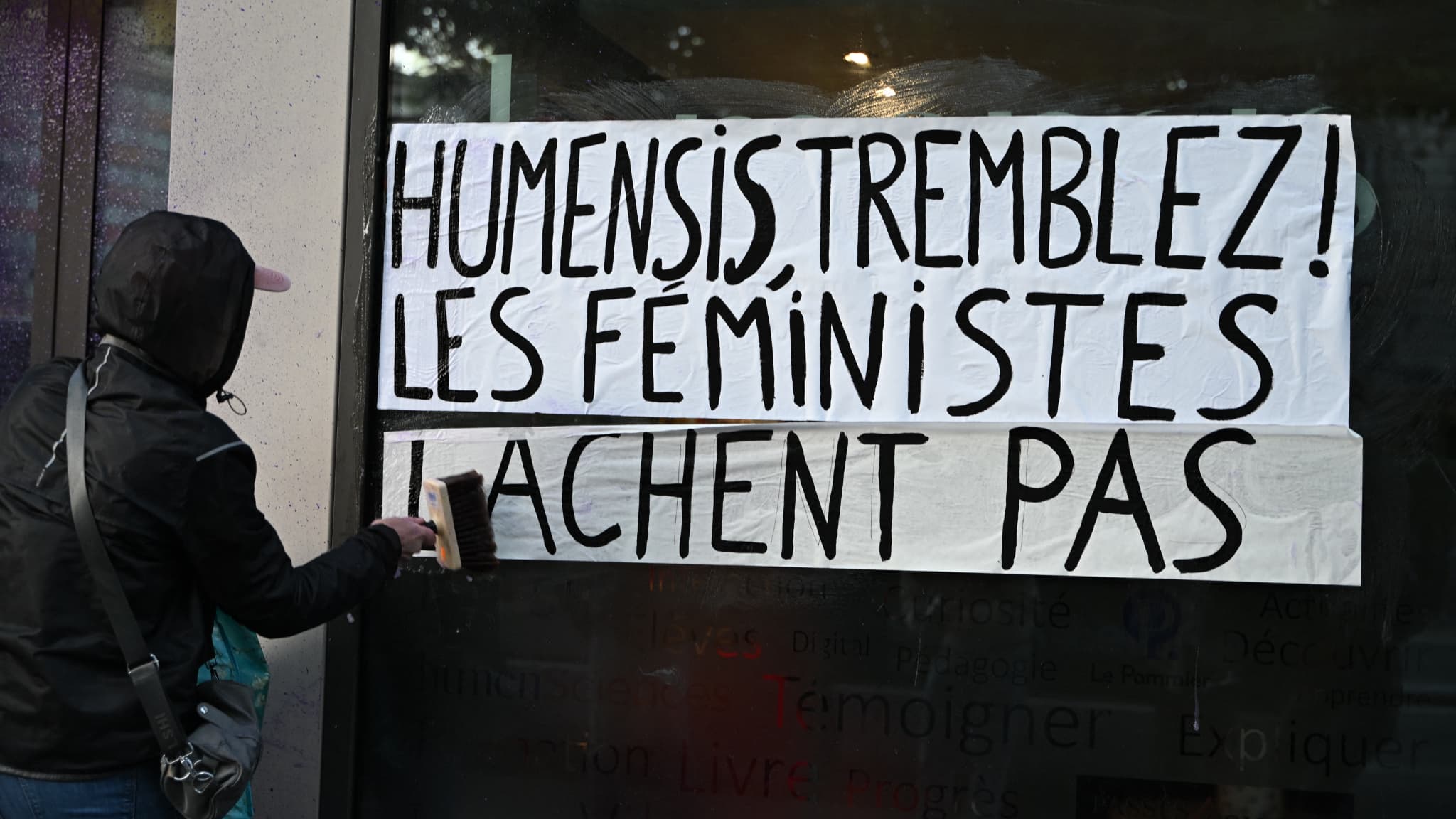 Une féministe colle une affiche sur la façade de Humensis Une féministe colle une affiche sur la façade de Humensis