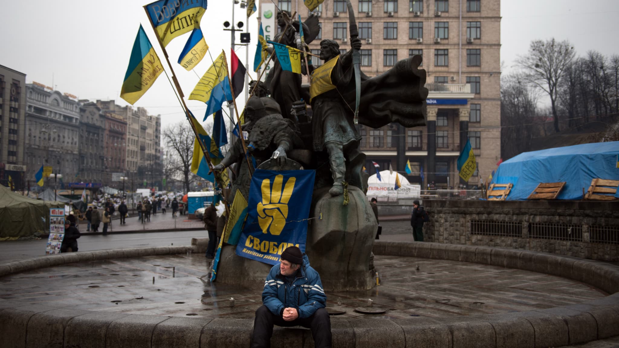 Un homme est assis sur une fontaine de la place Maïdan ornée d'une affiche du parti nationaliste ukrainien Svoboda et de drapeaux ukrainiens à Kiev, le 13 février 2014. 