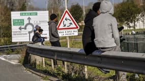Des migrant assis sur une barrière le long d'une route, proche de la ville de Calais, le 2 novembre 2017