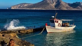 Illustration - Une femme assise à côté d'un bateau de pêche amarré sur la petite île égéenne de Koufonisi, dans la chambre des Cyclades, le 3 septembre 2021.
