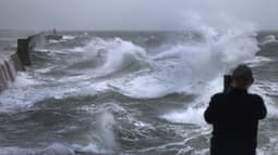 Un homme prend une photo avec son smartphone alors que d'énormes vagues et des vents violents causés par la tempête Benjamin frappent le port de Plobannalec-Lesconil, dans l'ouest de la France, le 22 octobre 2025.
