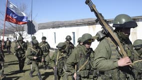 Un homme portant le drapeau russe salue des militaires en treillis qui bloquent l'accès à une base de la frontière ukrainienne à Perelvane, non loin de Simpferopol, le 3 mars 2014.