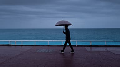 Un passant s'abrite de la pluie sous un parapluie, le long de la plage sur la "Promenade des Anglais" à Nice, le 30 octobre 2023