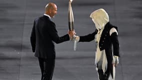 L'individu masqué transmet la flamme olympique à Zinédine Zidane lors de la cérémonie d'ouverture des Jeux de Paris 2024.