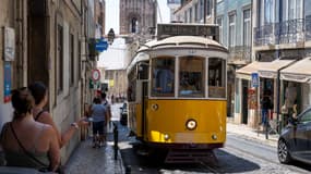 Des passants marchent près d'un tramway circulant dans une rue du quartier de Baixa à Lisbonne, au Portugal, le 4 août 2025.