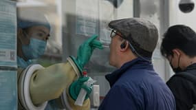 Une soigante prélève un échantillon par écouvillonnage sur un homme pour tester le coronavirus Covid-19 dans une station de collecte à Pékin, le 25 octobre 2021