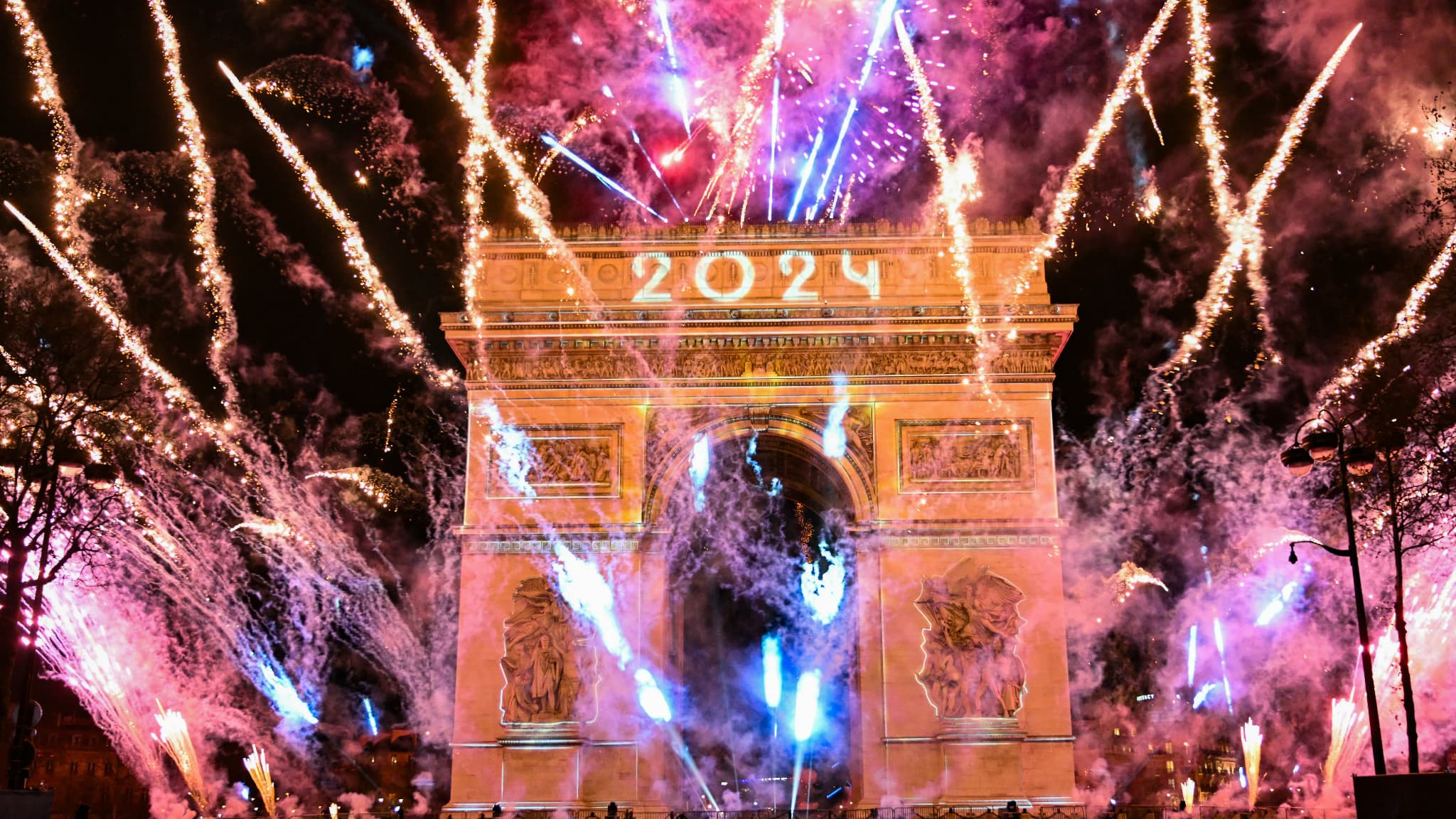 Des feux d'artifice explosent à côté de l'Arc de Triomphe avec "2024" projeté, sur l'avenue des Champs-Elysées pendant les célébrations du Nouvel An à Paris, au début du 1er janvier 2024.