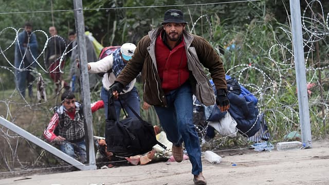 Un migrant traverse la frontière entre la Serbie et la Hongrie, après avoir fait un trou dans des barbelés.
