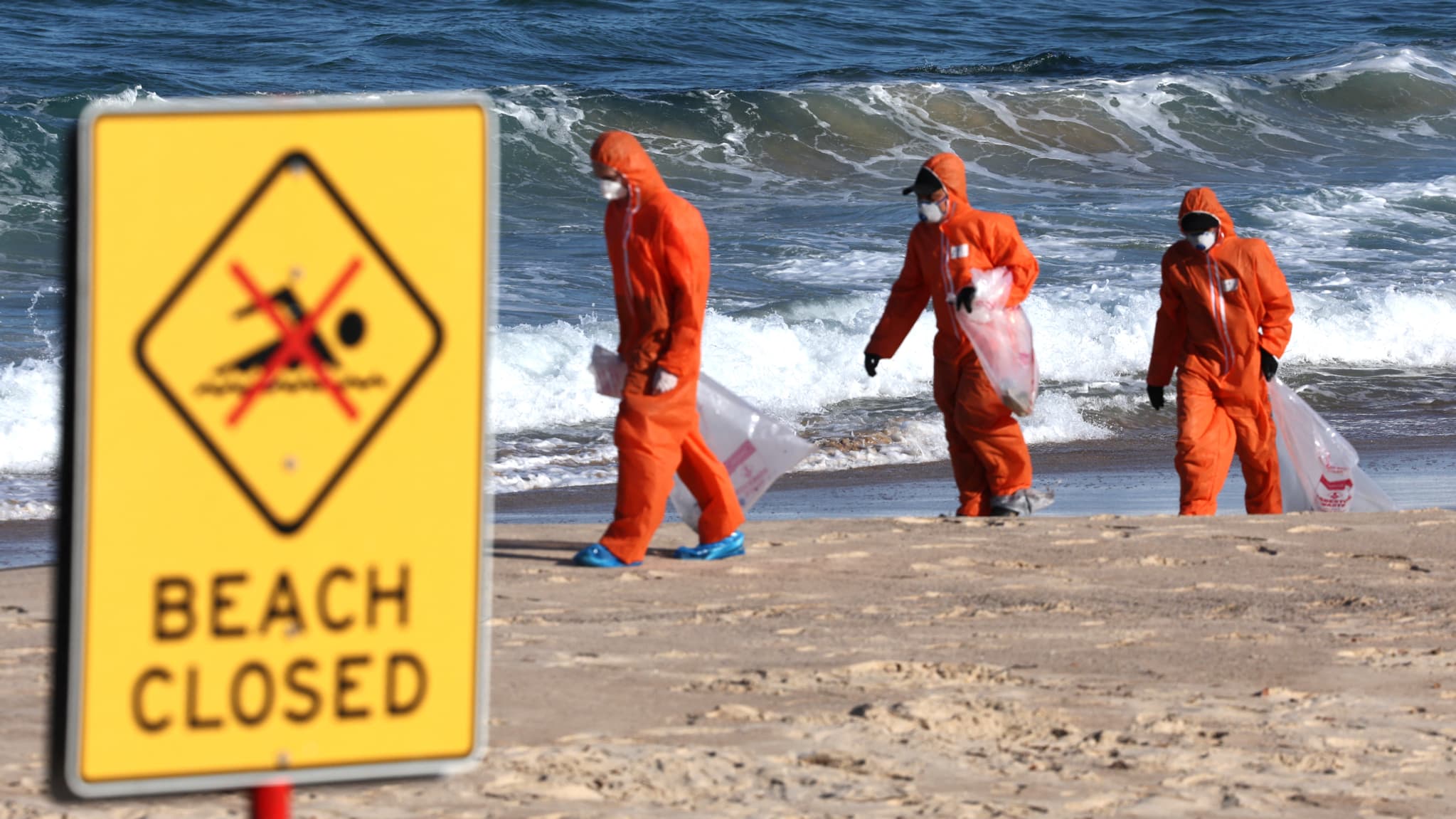 Des travailleurs en combinaison de protection mènent une opération de nettoyage pour éliminer les « boules de goudron » à base de pétrole échouées sur la plage de Coogee à Sydney, le 17 octobre 2024. 