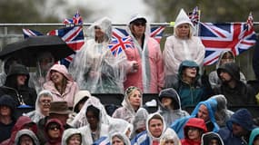 Des spectateurs attendent la procession du roi sous une pluie diluvienne, le 6 mai 2023, à Londres.