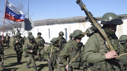 Un homme portant le drapeau russe salue des militaires en treillis qui bloquent l'accès à une base de la frontière ukrainienne à Perelvane, non loin de Simpferopol, le 3 mars 2014.