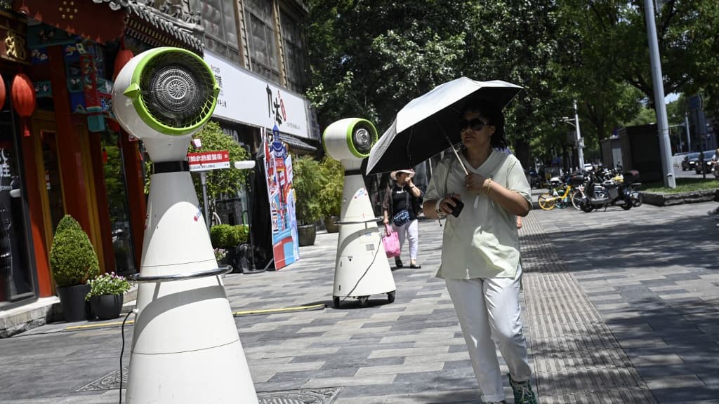 Dans la rue, une femme se protège du soleil avec un parapluie devant un ventilateur de refroidissement, à Pékin, le 6 juillet 2023.