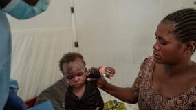 Un enfant aidé par sa mère sous le regard d'un agent de santé au centre de traitement du Mpox à l'hôpital général de référence de Nyiragongo, au nord de Goma, le 17 août 2024.