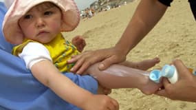 Une personne applique de la crème solaire sur les jambes d'une petite fille, le 27 mai 2001 sur la plage de Cabourg.
