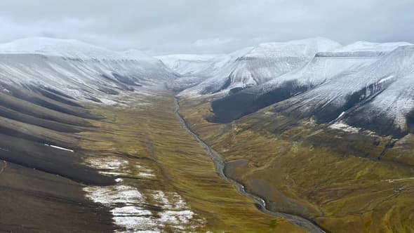 Une vue aérienne prise depuis un hélicoptère montre des montagnes enneigées et une rivière dans une vallée de l'archipel arctique norvégien du Svalbard, au nord de la Norvège, le 13 septembre 2023.
