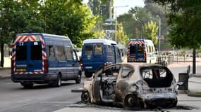Des véhicules de police passent à proximité d'une voiture incendiée dans le quartier des Grésilles, le 15 juin 2020 à Dijon