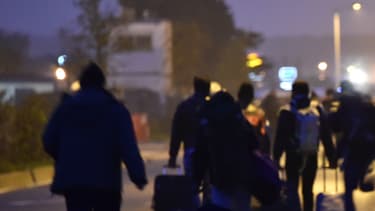 Des migrants passent avec leurs bagages devant un panneau "Calais, le 24 octobre 2016.