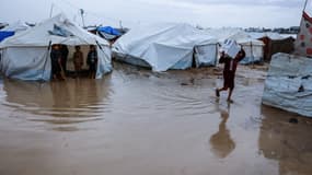 Un garçon transporte une boîte à travers une flaque d'eau dans un camp de fortune abritant des Palestiniens déplacés après de fortes pluies dans le quartier de Zeitoun, à Gaza, le 11 décembre 2025.