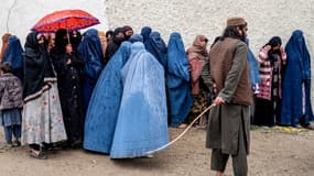Un membre des forces de sécurité talibanes monte la garde tandis que des femmes afghanes vêtues de burqas font la queue sous une pluie battante pour recevoir des denrées alimentaires données pendant le mois sacré du ramadan, à Kaboul, le 25 mars 2025. (Photo d'illustration)