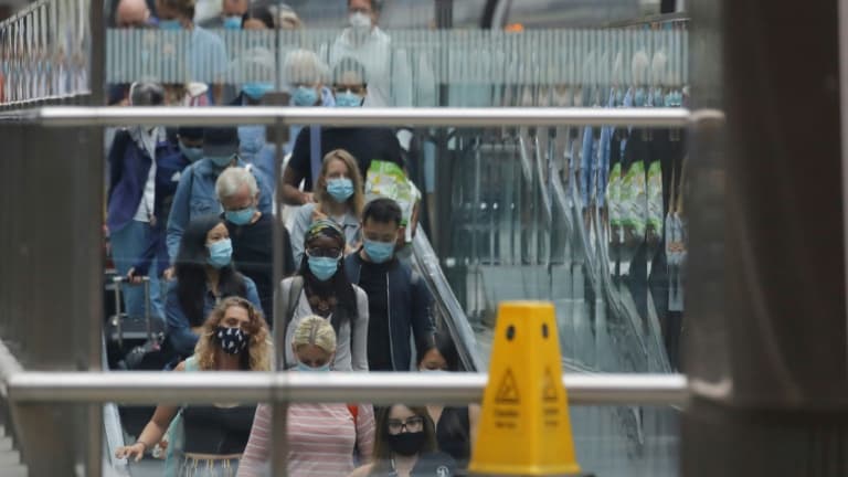 Des voyageurs, portant des masques de protection, prennent un escalator à leur descente de l'Eurostar en provenance de Paris, le 14 août 2020 à la gare St Pancras de Londres