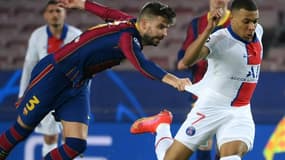 Le défenseur espagnol de Barcelone, Gerard Piqué (g), retient l'attaquant français du Paris-SG, Kylian Mbappé, lors du 8e de finale aller de la Ligue des champions face au FC Barcelone, au Camp Nou, le 16 février 2021