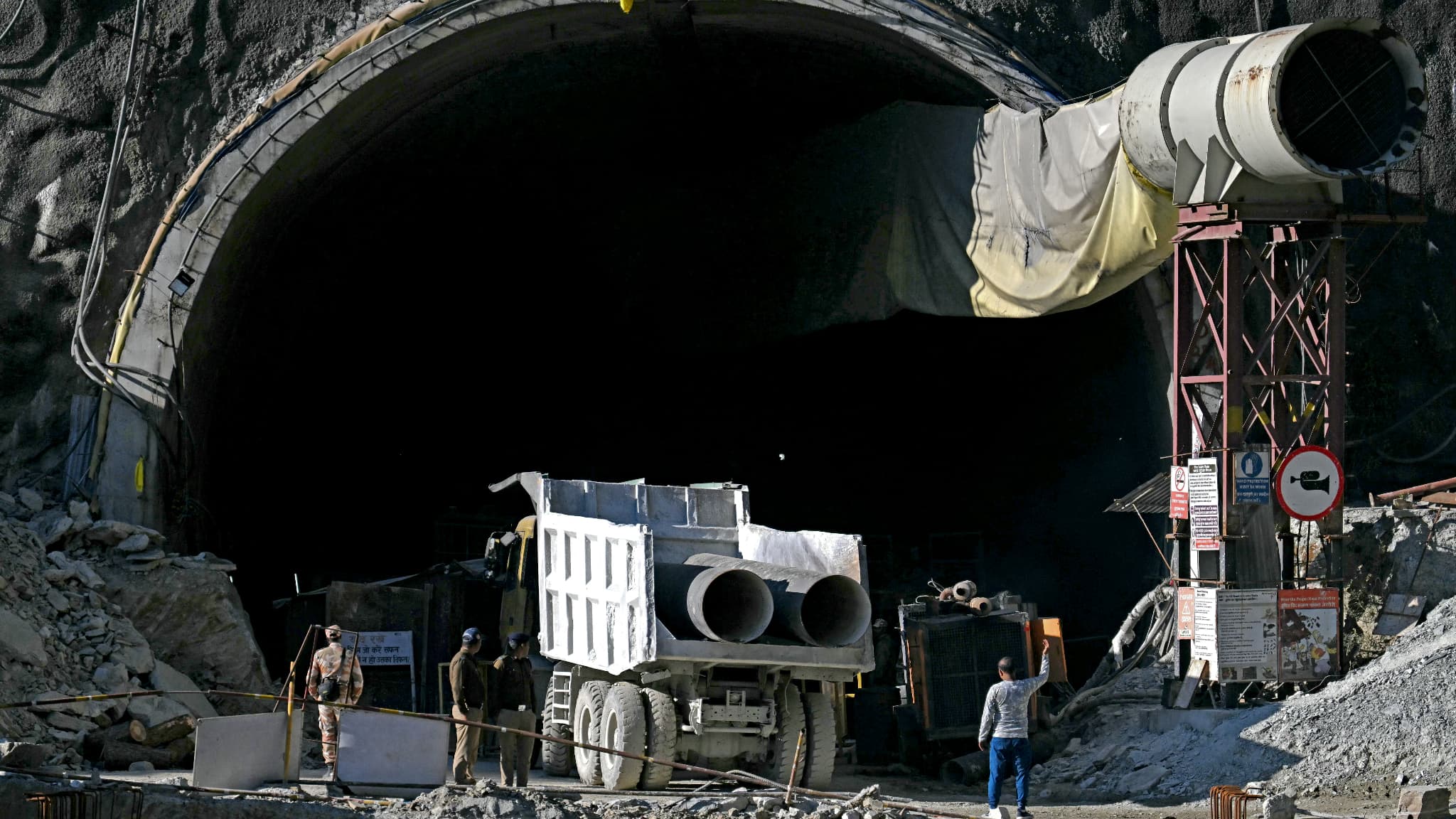 Le personnel de sécurité observe un camion transportant des tubes métalliques à travers l'entrée du tunnel routier en construction de Silkyara, quelques jours après son effondrement dans le district d'Uttarkashi de l'État indien de l'Uttarakhand, le 21 novembre 2023.