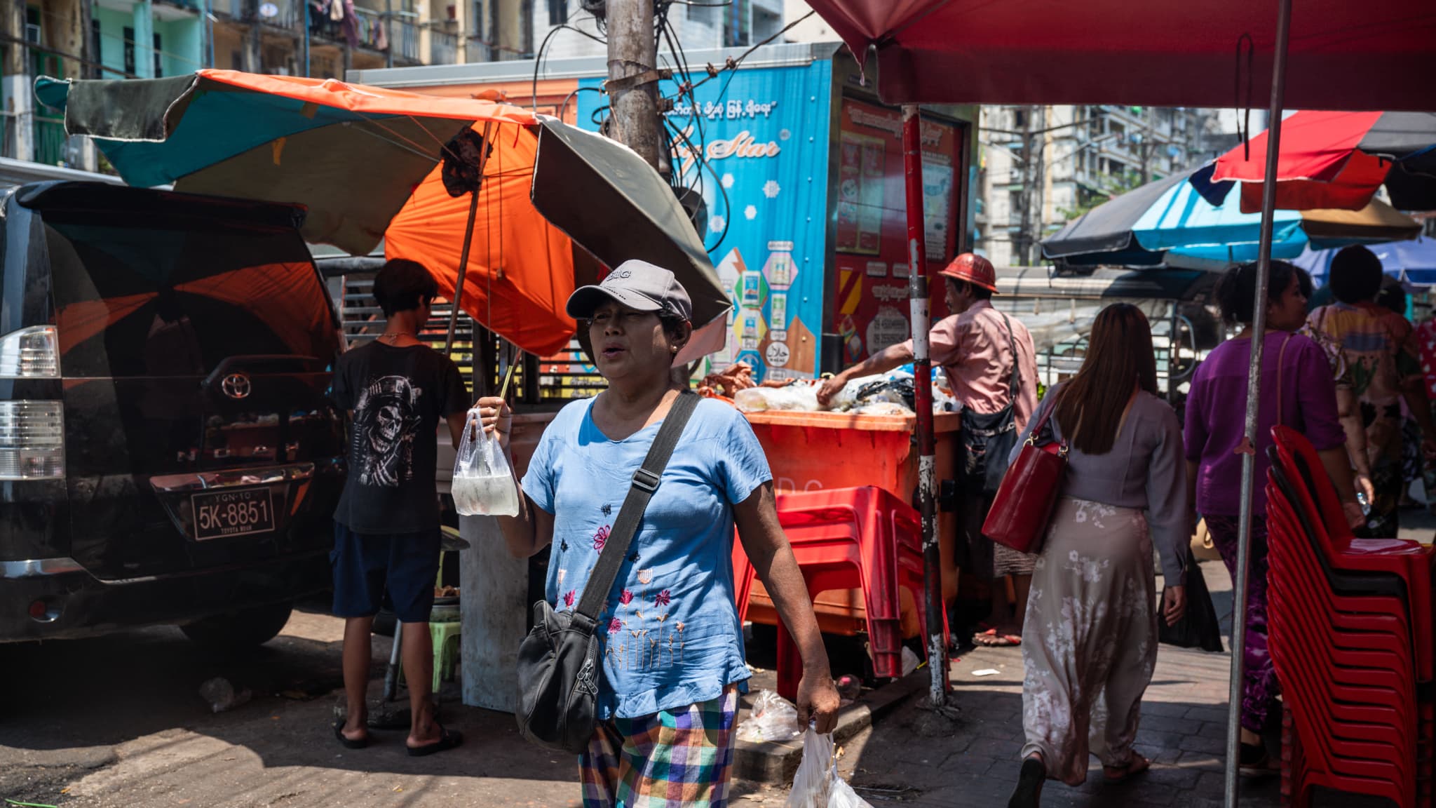 Une femme se promène avec une boisson fraîche sous un parapluie le long d'une rue par une chaude journée à Yangon le 25 avril 2024. 