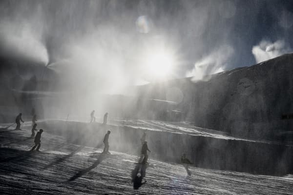 Des skieurs passent à travers la neige d'un canon à neige à la station française de Val Thorens le jour de son ouverture, le 26 novembre 2022.