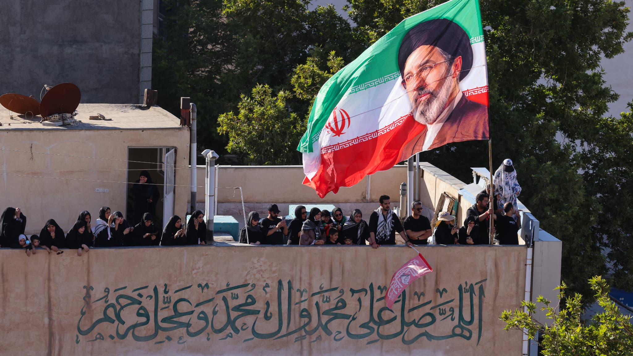 Un drapeau iranien à l'effigie du guide suprême actuel, Mojtaba Khamenei, au sommet d'un immeuble tandis que la foule assiste aux funérailles du guide suprême assassiné, Ali Khamenei, et de sa famille, à Mashhad, le 9 juillet 2026.