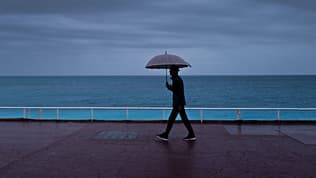 Un passant s'abrite de la pluie sous un parapluie, le long de la plage sur la "Promenade des Anglais" à Nice, le 30 octobre 2023
