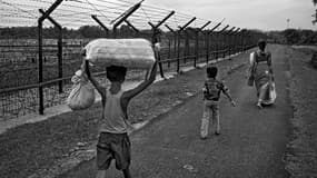 Dans la région de Balurghat, en Inde, une mère et ses deux enfants vont rendre visite à des membres de leur famille habitant dans un village voisin, également installé à proximité de la clôture.