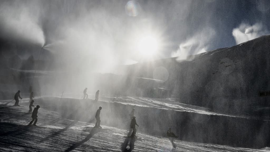 Des skieurs passent à travers la neige d'un canon à neige à la station française de Val Thorens le jour de son ouverture, le 26 novembre 2022.