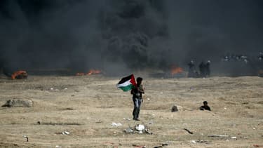 Un homme tient un drapeau palestinien lors d'affrontements avec les forces israéliennes, près de la frontière entre Gaza et Israël, le 14 mai 2018.