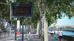 Des piétons à prpximité d'un panneau municipal alertant de la canicule en cours, le 18 août 2023 à Lyon