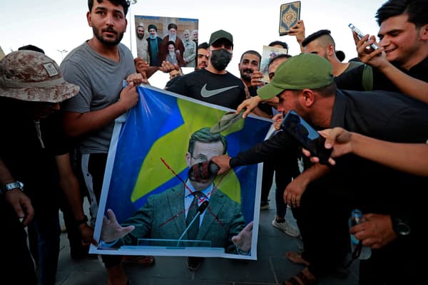 Des partisans de l'ancien groupe paramilitaire Hashd al-Shaabi tiennent une affiche représentant le Premier ministre suédois Ulf Kristersson avec un grand X dessiné dessus lors d'une manifestation sur la place Tahrir de Bagdad le 20 juillet 2023.