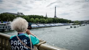 Une bénévole des JO-2024 prend une photo sur le pont des Invalides à côté des tribunes installées sur la Seine à la veille de la cérémonie d'ouverture des Jeux Olympiques 2024, à Paris, le 25 juillet 2024