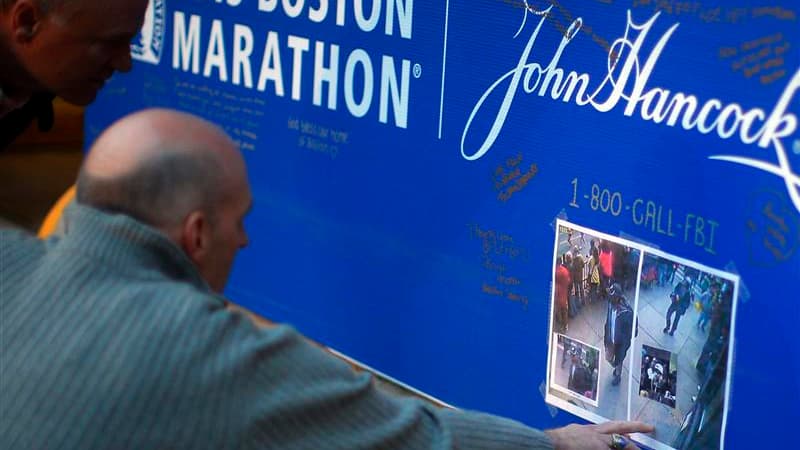 A Boston deux hommes regardent les photos de deux suspects dans l'enquête sur le double attentat à la bombe de Boston diffusées par le FBI jeudi. /Photo prise le 18 avril 2013/REUTERS/Brian Snyder