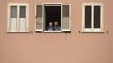 Image d'illustration - Deux personnes regardant dehors depuis leur fenêtre - Tiziana FABI / AFP