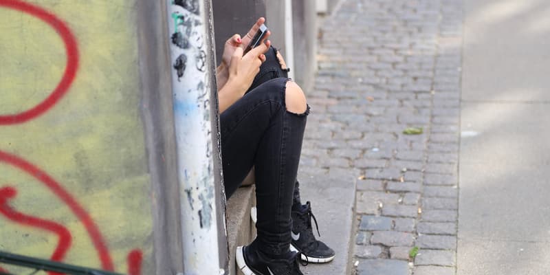 Une adolescente assise sur un pas de porte, en train d'écrire sur son smartphone (Photo d'illustration).