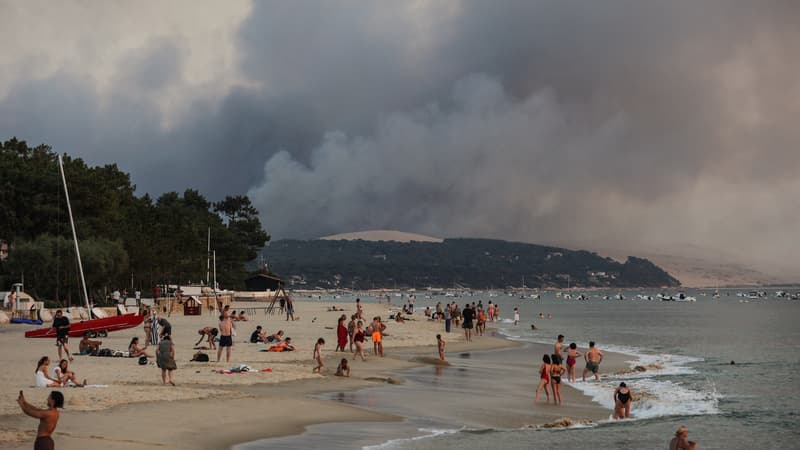 Cette photo prise le 18 juillet 2022 montre des personnes se baignant sur la plage du Moulleau alors que de la fumée s'élève de l'incendie de forêt de La Teste-de-Buch, vue d'Arcachon, devant la dune du Pilat. 