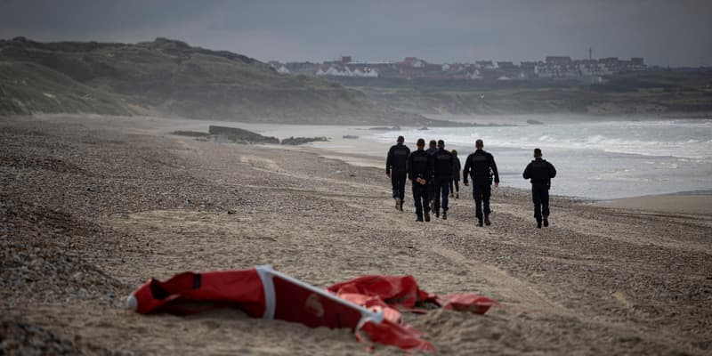 Des policiers français patrouillant sur la plage entre Ambleteusse et Wimereux, dans le nord de la France, passent devant l'épave d'un bateau pneumatique utilisé par des migrants qui tentent de traverser la Manche vers l'Angleterre, le 16 octobre 2021. 
