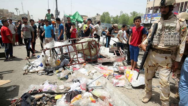 Un membre des forces de sécurité irakiennes monte la garde, alors que les civils regardent les dégâts causés par l'attaque de Daesh, dans un marché de Bagdad, le 11 mai 2016.