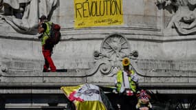 Des manifestants se tiennent à côté d'une banderole "Révolution" et "Oligarchie dégage" sur la place de la République à Paris, le 20 avril 2019 à l'occasion du 23e samedi de mobilisation des gilets jaunes. 